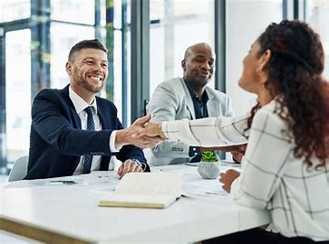 Business partners meeting across a desk, exchanging a firm handshake with focused expressions—representing trust, shared goals, and the start of a meaningful collaboration