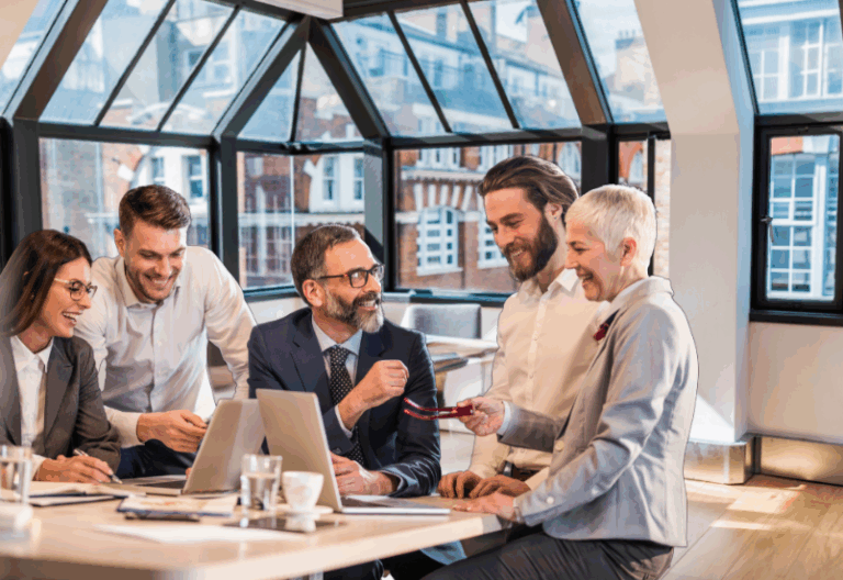 Five diverse team members seated around a table, smiling and laughing during a collaborative meeting.